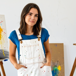 ** A professional female artist in a modest, paint-splattered overall dress, standing in a bright, airy art studio, surrounded by canvases and paintbrushes. Fully clothed, appropriate content, safe for work. Perfect anatomy, correct proportions, natural pose, well-formed hands, proper finger count, natural body proportions, professional photography, high quality.

**